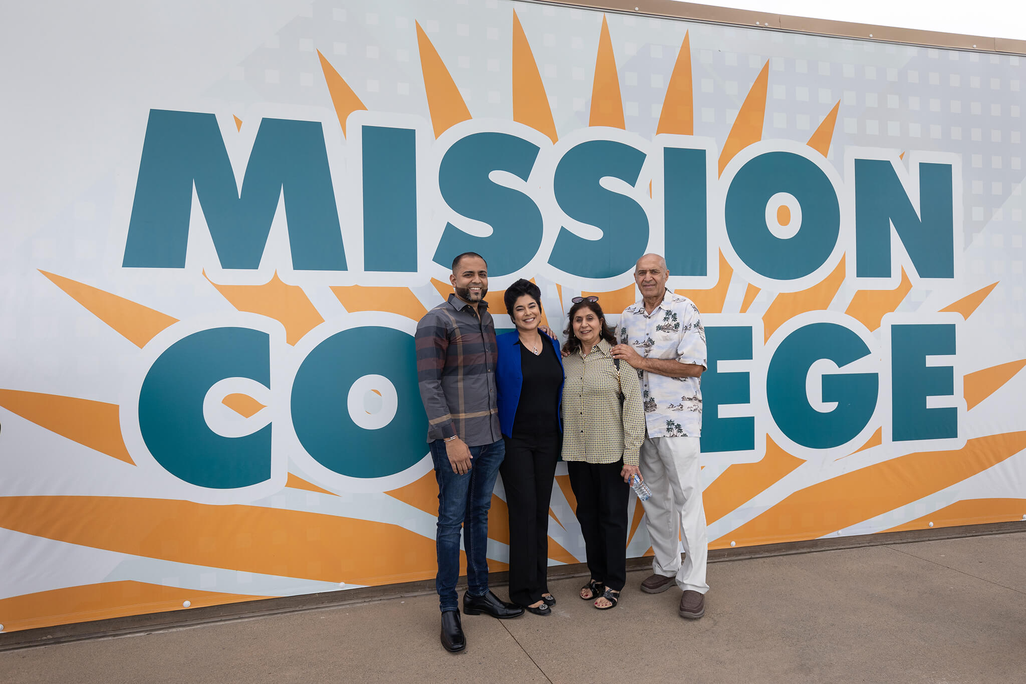 Seher Awan posing for picture with others in front of a wall that has a Mission College banner over it. 